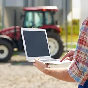 Agricultor con laptop en el campo, representando la digitalización y transformación tecnológica en zonas rurales.