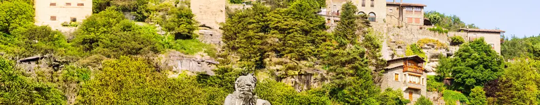 Vista de un pueblo con arquitectura tradicional rodeado de vegetación y una estatua en primer plano.